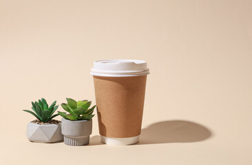 Craft cardboard disposable coffee cup and decorative plant on beige background with shadow....