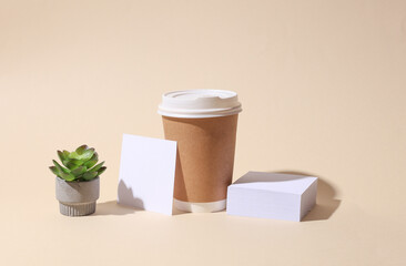 Craft cardboard disposable coffee cup and white square memo card on beige background with shadow. Minimalistic scene