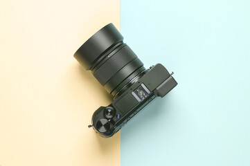 Modern digital mirrorless camera with a lens on a blue-yellow pastel background. Top view. Minimalism