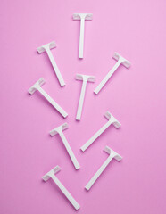 Disposable white plastic razors on pink background. Top view
