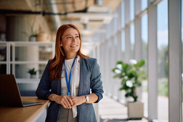 Happy female manager using laptop while working in office and looking away.