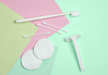 White razor with cotton pads and sticks, toothbrush on pastel background. Self-hygiene, beauty concept. Top view. Flat lay