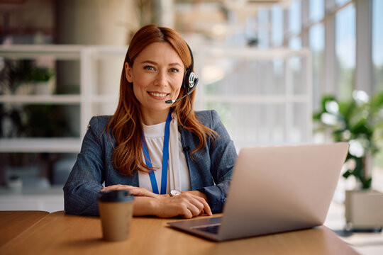 Happy businesswoman with headset using laptop in office and looking at camera. - Powered by Adobe