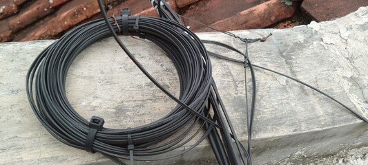 Roll of Fiber Optic Cable Stored on Upper Balcony, Coiled Black Wire in Outdoor Setting,...
