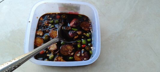 Traditional Indonesian Spicy Soy Sauce Condiment with Shallots and Chili Peppers in a Plastic Container – Sambal Kecap Close-Up Top View