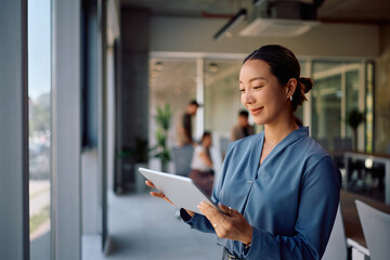 Happy Korean businesswoman working on digital tablet in office.