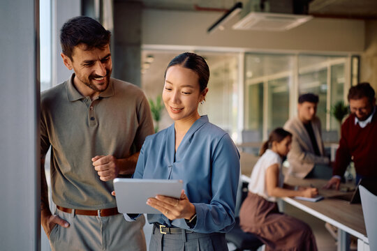Happy diverse coworkers using touchpad while working in office. - Powered by Adobe