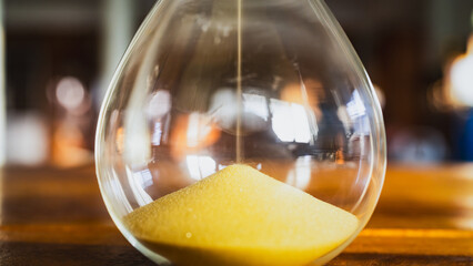 Hourglass with focus on sand on which side is placed on table. Concept of spending time relaxing with nature, caring for the environment.