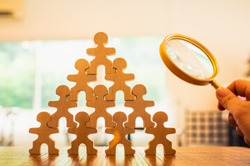 A magnifying glass and wooden figures with business hand search for someone who ‘s special person. Concept of Human resources management and recruitment.