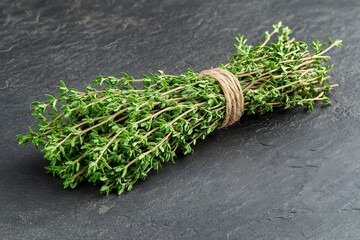 Fresh thyme bunch tied with rustic twine lies on a textured dark surface above