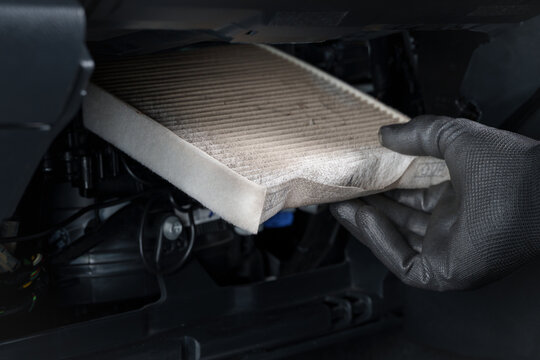 Mechanic Replacing a Dirty Cabin Air Filter in a Car Interior.Close-up of a gloved hand removing a dirty cabin air filter from a car 