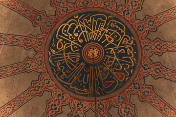 Ornate ceiling of mosque featuring arabic calligraphy and geometric patterns