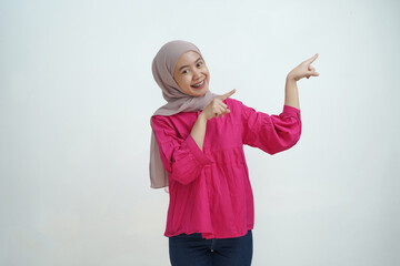 Smiling Young Asian Muslim Woman in Hijab Pointing with Both Hands on isolated background