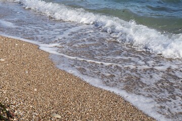 Close-up of gentle sea wave rolling on sandy shore. Sparkling sea water and foam on shore at sunset