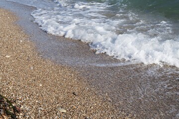 Close-up of gentle sea wave rolling on sandy shore. Sparkling sea water and foam on shore at sunset