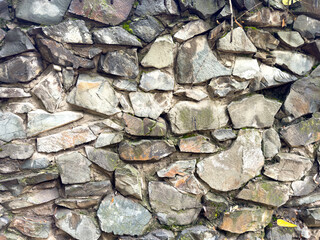 Texture of an old stone wall made of rough rocks with moss and cracks. Natural stone background.
