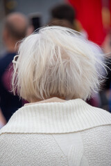 A woman with a white sweater and glasses is sitting in a crowd