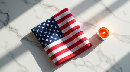 Folded american flag and a small candle casting shadows on a white marble surface