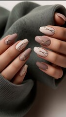 elegant nude-pink manicured nails and a gold ring adorned with a heart-shaped gemstone, complemented by a cozy white sweater sleeve.