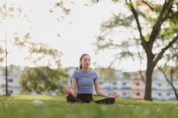 A young woman in workout attire practices yoga in a peaceful pose at a public park. The soft...