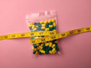 Top view of a medicine pill package with measuring tape on a pink background