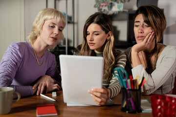 Group of diverse young women looking at a tablet with serious and concerned expressions.