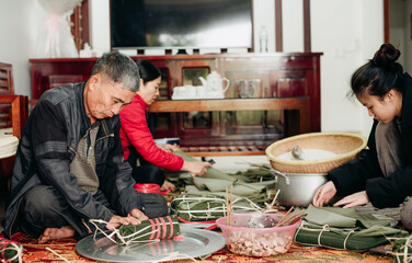 Family working together to prepare traditional food using bamboo leaves in a cozy indoor setting...