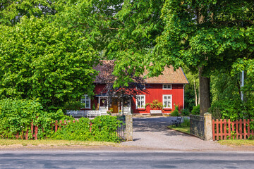 Entrance from a road to a red idyllic house with a wooden fence
