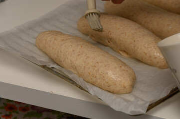 A woman gently brushes homemade Graham loaves with egg wash before placing them in the oven.