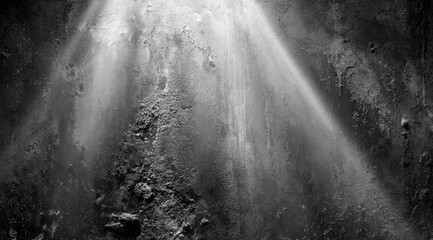 A grayscale image shows a textured wall, possibly concrete, dramatically lit from above by a spotlight creating converging beams of light and shadow, highlighting the wall's rough and decaying surface