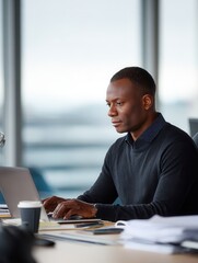Focused african male adult working on laptop in modern office setting.