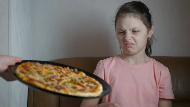 Child refuse from pizza. A view of emotional young girl refuse to takes fast food pizza in the room.