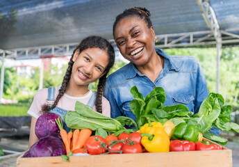 Black farmer mother and daughter holding basket with produce and laughing happily at vegetable farm...