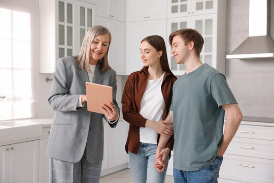 Smiling real estate agent with tablet working with couple in kitchen - Powered by Adobe