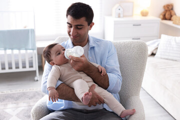 Father feeding his little baby with bottle on armchair at home