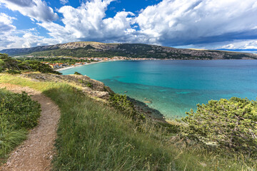 Obraz premium Green grass in a clearing, rest on a trail near the town of Baska, view of the bay and the city panorama