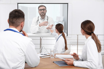 Team of doctors using video projector during conference indoors. Speaker on projection screen