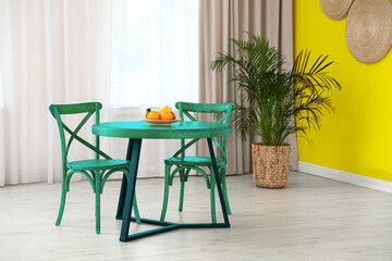 Turquoise dining table and chairs near yellow wall in room. Interior design