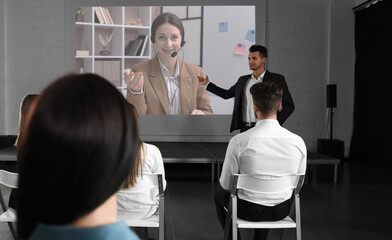 Group of people participating in business conference indoors. Speaker on projection screen