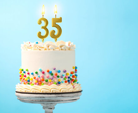 Yummy cake with sprinkles and burning number shaped candles on light blue background, space for text. 35th birthday or other special occasion