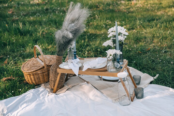 Elegant picnic setup on lush green grass with decorative flowers and unique tableware