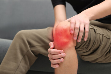 Man suffering from pain in knee on sofa at home, closeup