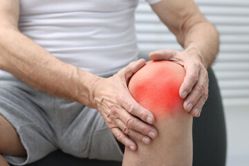 Senior man suffering from pain in knee at home, closeup