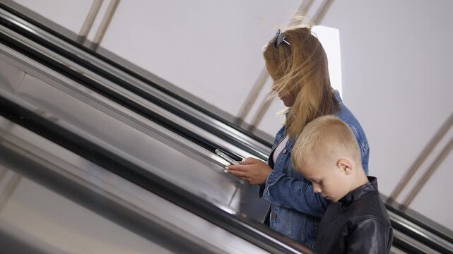 Mother and son are seen climbing the escalator in the subway, both holding phones in their hands. This is a sign of telephone addiction.