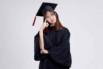 College degree graduations. Young Asian girl in gown with mortarboard thinking isolated on white...