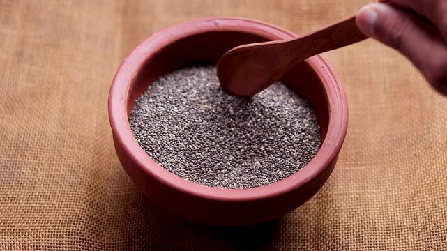 Chia seeds in a bowl with a wooden spoon in it . Healthy vegan superfood. Hand pours chia seeds. Falling chia seeds. Rustic wooden table. Top view, flat lay. 4k video