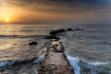 Sunrise over alicante beach with waves crashing on stone jetty