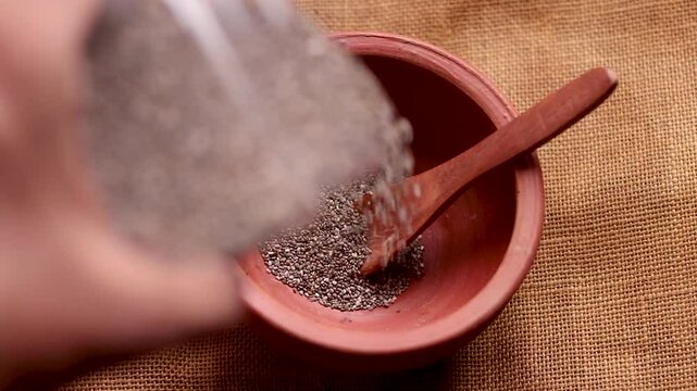 Chia seeds falling in wooden bowl in slow motion. Healthy vegan superfood. Hand pours chia seeds. Falling chia seeds. Rustic wooden table. Top view, flat lay. 4k video