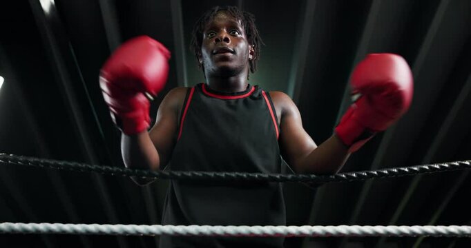 Fitness, boxing ring and man on rope for rest, relax or getting ready for challenge with low angle. Black person, tired boxer and break in gym with breathing, fatigue or motivation for fight or sport