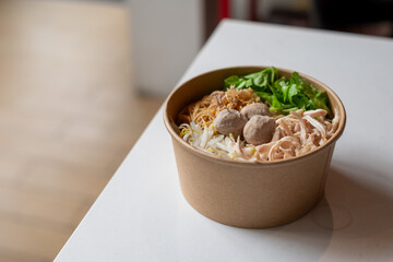 Delicious Noodle Soup with Meatballs and Fresh Herbs in a Paper Bowl